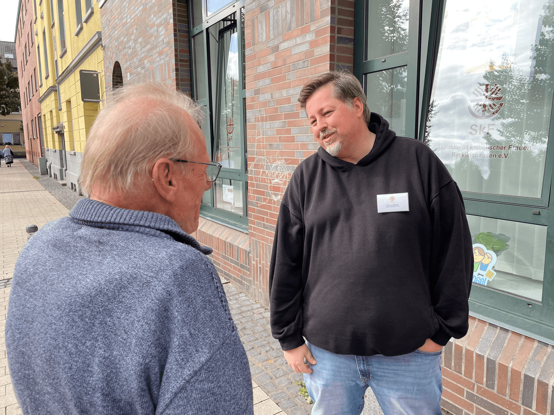 Der Stadtteilmanager des SkF Recklinghausen Denis Köhler steht mit schwarzen Pullover bekleidet einem anderen Mann gegenüber