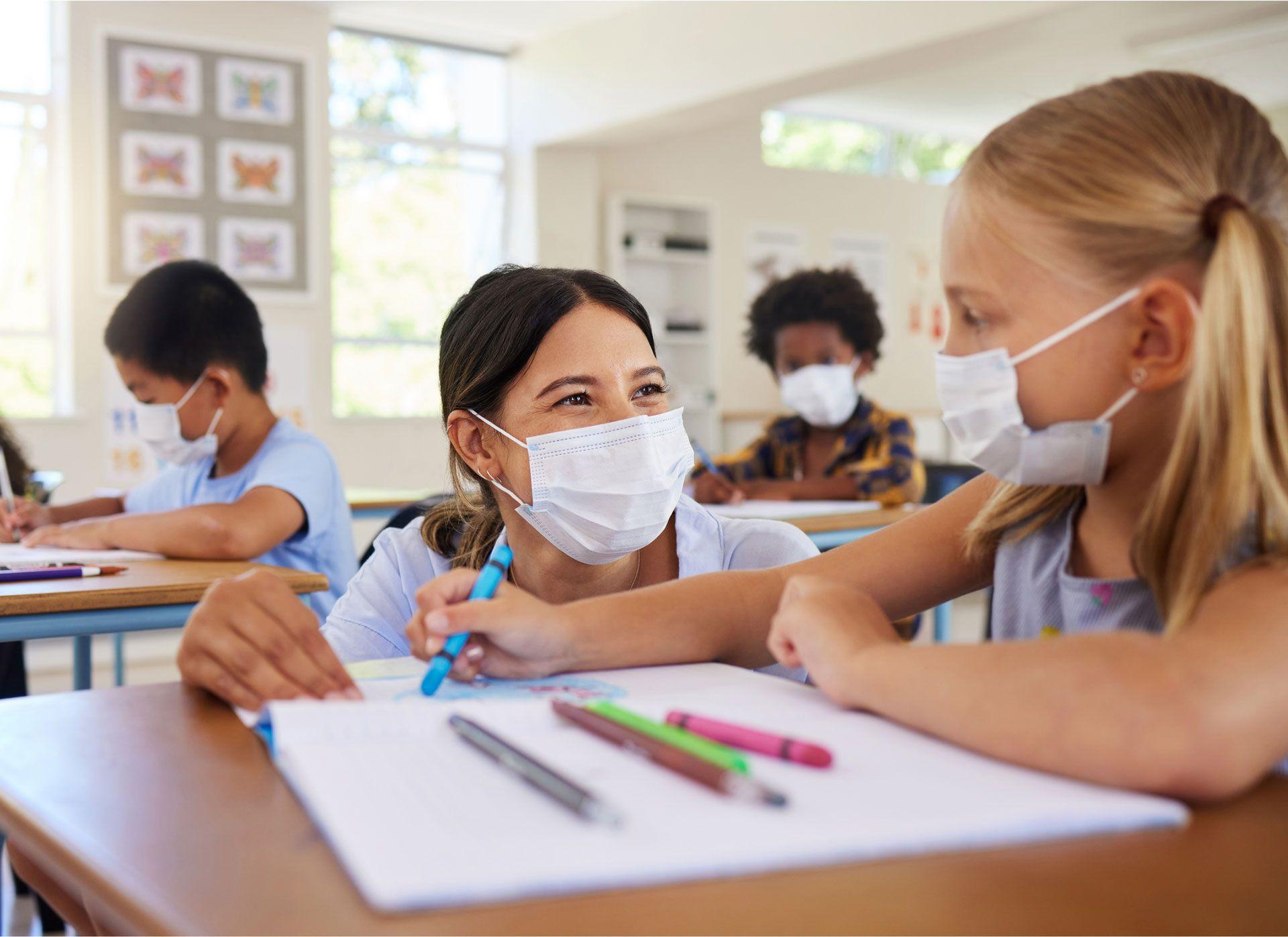 Kinder mit Schutzmasken sitzen in einem Klassenzimmer und arbeiten gemeinsam an Schulaufgaben – ein Symbol für Bildung während der Pandemie.