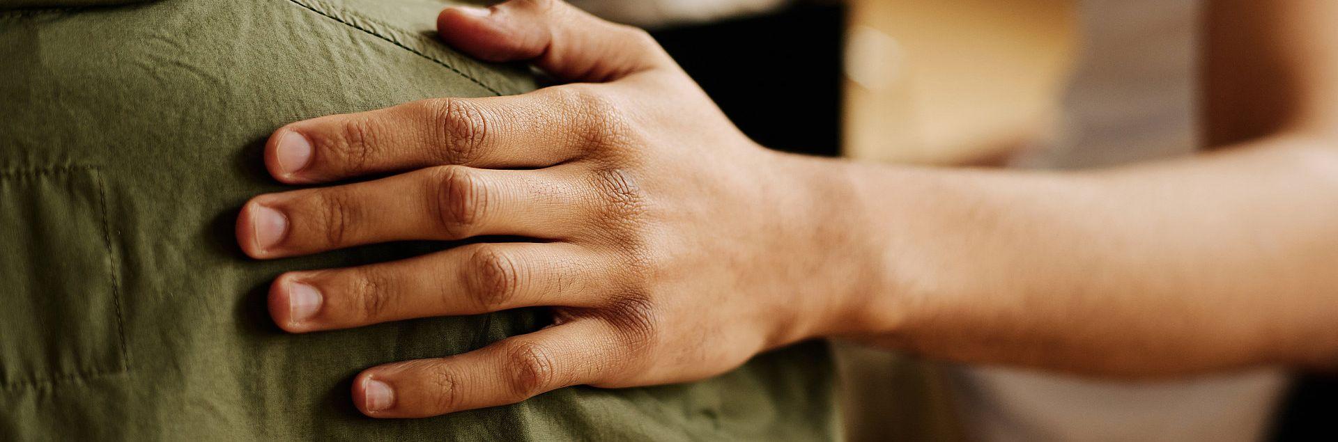 Eine unterstützende Hand liegt auf der Schulter einer Person in einer grünen Jacke – ein Symbol für Mitgefühl, Unterstützung und Zusammenhalt.