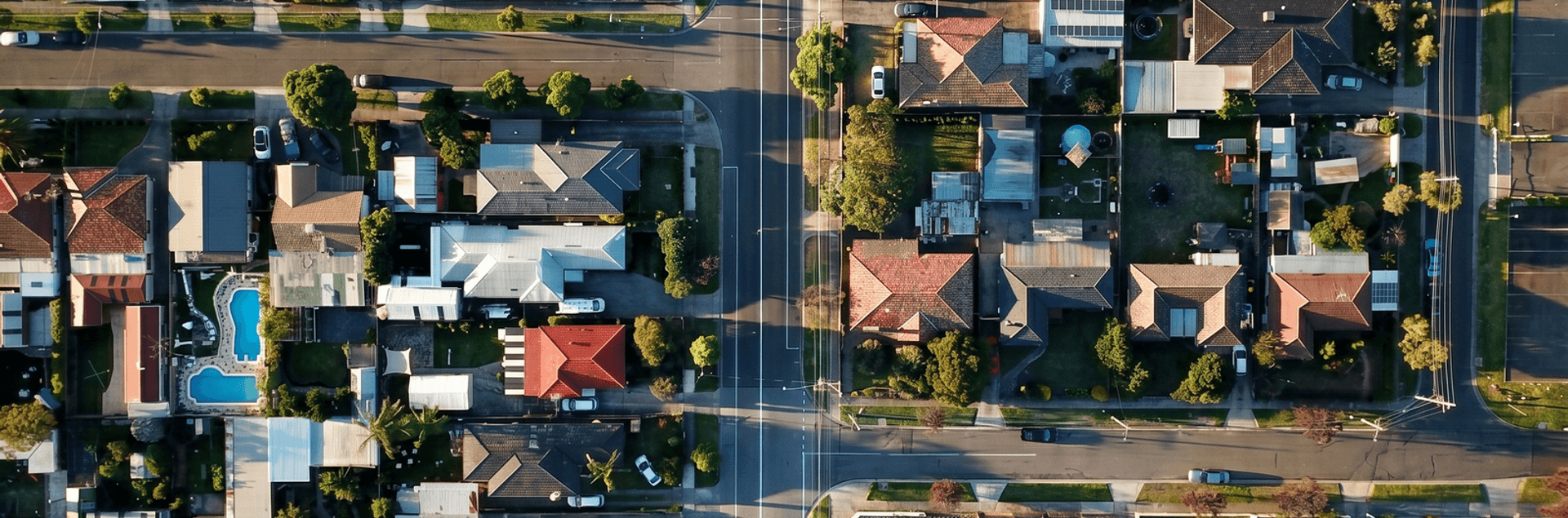 Luftaufnahme eines Wohnviertels mit zahlreichen Einfamilienhäusern, Gärten und Straßenkreuzungen. Die Dächer der Häuser sind in verschiedenen Farben gehalten, einige mit Solaranlagen ausgestattet.