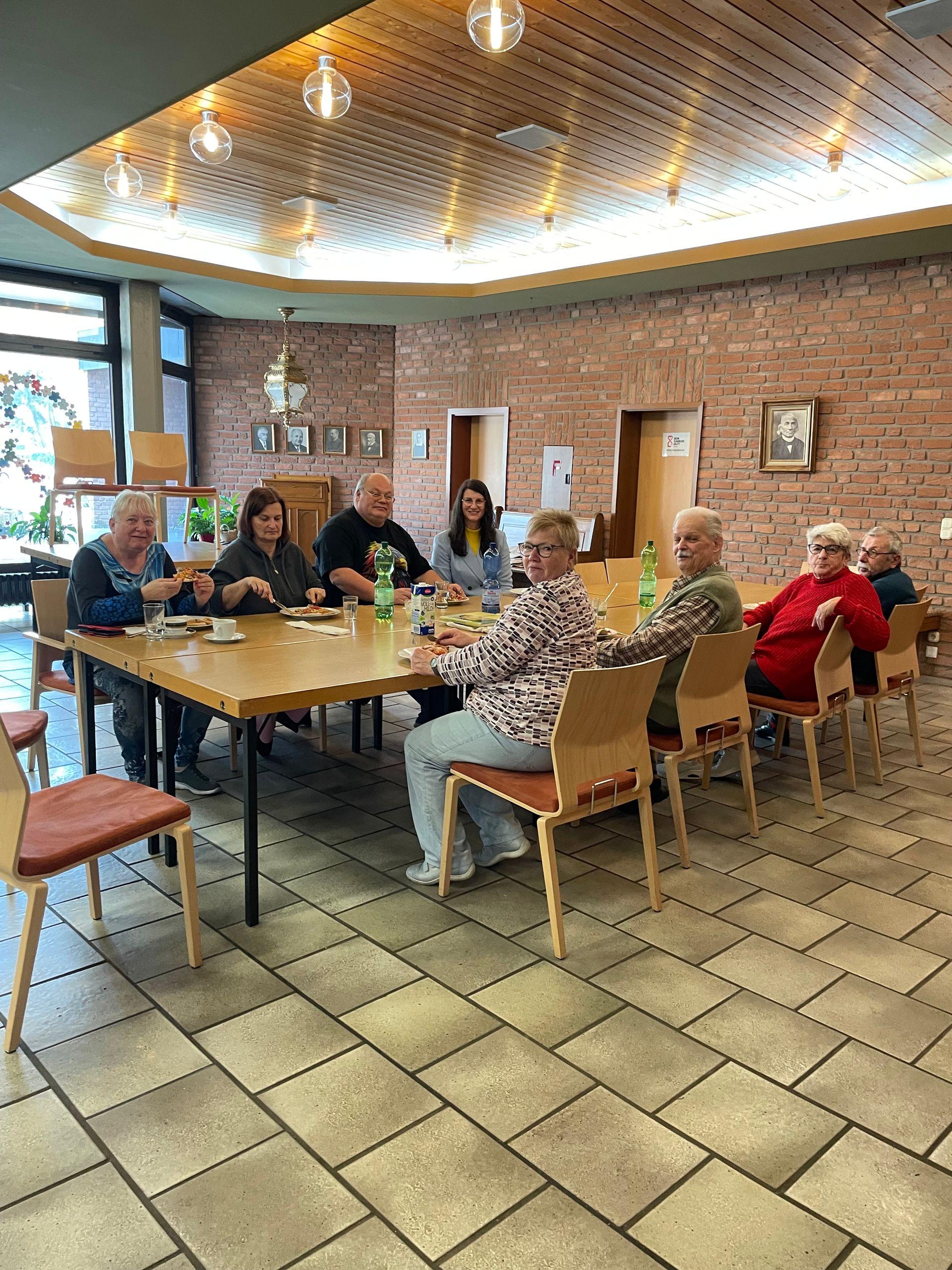 Eine Gruppe von Senior:innen sitzt versammelt um einen großen Tisch und essen gemeinsam. Eine Gruppe von Senior:innen sitzt versammelt um einen großen Tisch und essen gemeinsam.