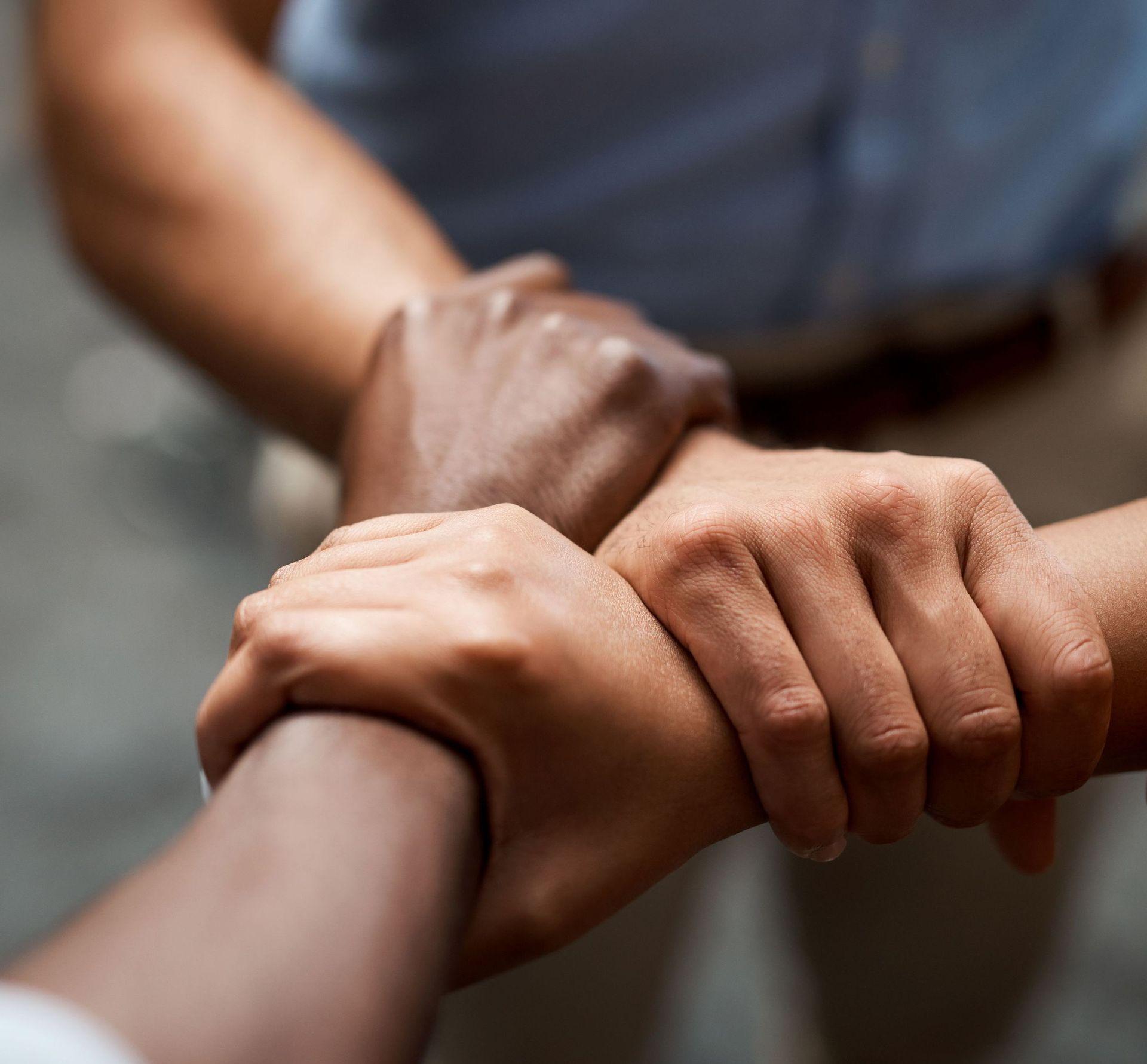 Drei Menschen fassen sich gegenseitig mit einem Arm an den Handgelenken Drei Menschen fassen sich gegenseitig mit einem Arm an den Handgelenken