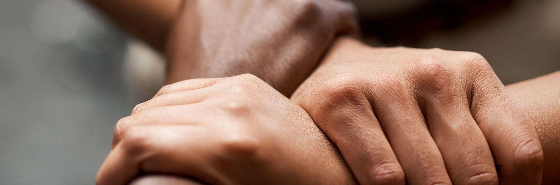 Drei Menschen fassen sich gegenseitig mit einem Arm an den Handgelenken Drei Menschen fassen sich gegenseitig mit einem Arm an den Handgelenken