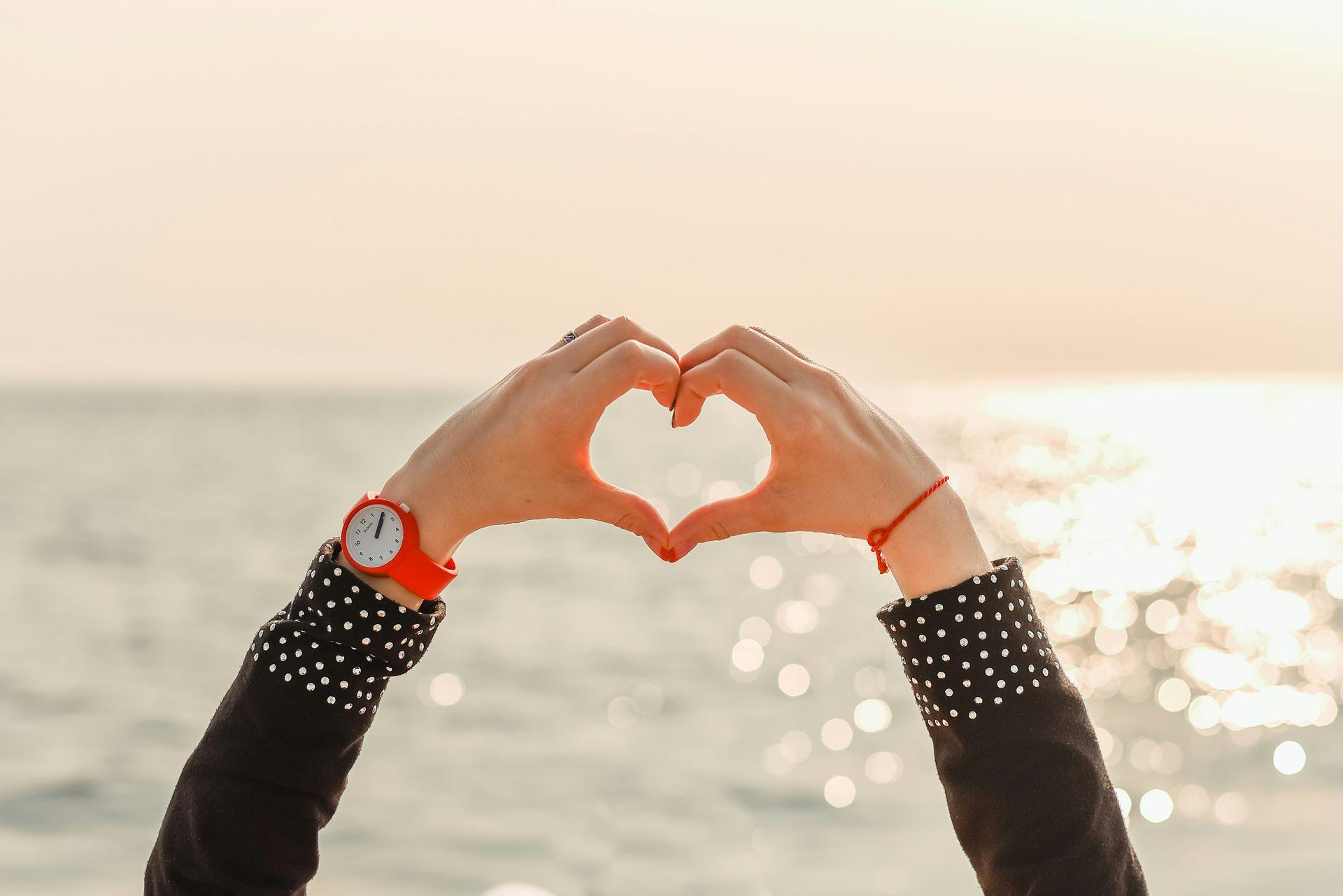 Eine Person formt ein Herz mit Ihren Händen vor dem Hintergrund eines Meeres Eine Person formt ein Herz mit Ihren Händen vor dem Hintergrund eines Meeres